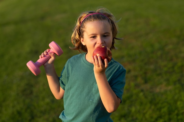 Gezond sportief kind met appel en halter buiten in het park Kid opvoeden van een halter Schattig kind training met halters Kids fitness Kid jongen trainen met halters Gezonde kinderen