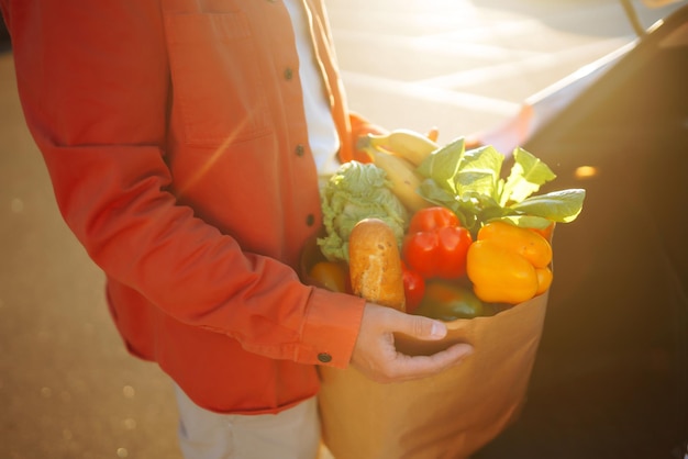 Gezond veganistisch vegetarisch eten in een papieren zak in de mannelijke handen Man met boodschappentas bij de auto