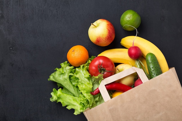 Gezond vegetarisch eten in een papieren zak groenten en fruit op een donkere achtergrond