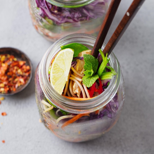 Gezonde aziatische salade met noedels, groenten, kip en tofu in glazen potten Grijze achtergrond Close-up