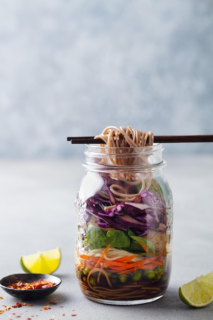 Gezonde aziatische salade met noedels, groenten, kip en tofu in glazen potten Grijze achtergrond Kopieer ruimte