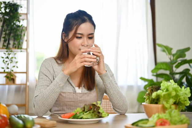 Gezonde Aziatische vrouw die een glas water drinkt en nipt in de keuken voordat ze gaat eten