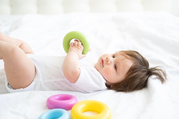 Gezonde babyjongen liggend op bed en spelen met kleurrijke plastic cirkel speelgoed.