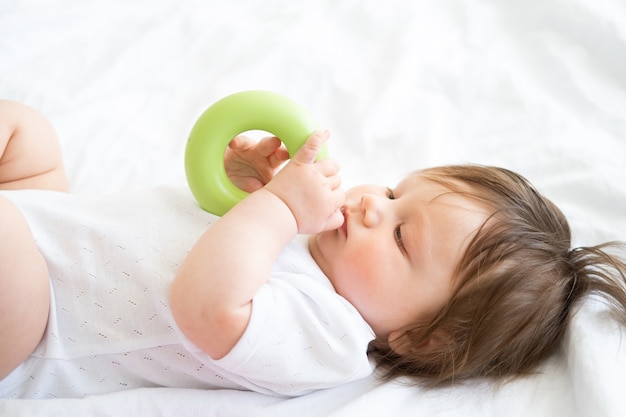 Gezonde babyjongen liggend op bed en spelen met kleurrijke plastic cirkel speelgoed.