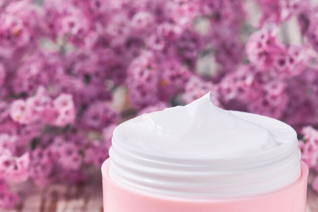 Gezonde cosmetische crème met kruiden gezichtsverzorging of vochtlotion, close-up. Plastic roze pot voor gevoelige huidcrème op een houten tafel.