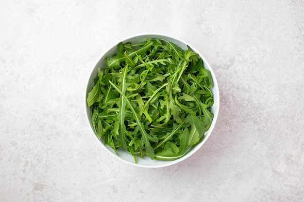 Gezonde en frisse salade met rucola in een witte kop op lichte achtergrond.