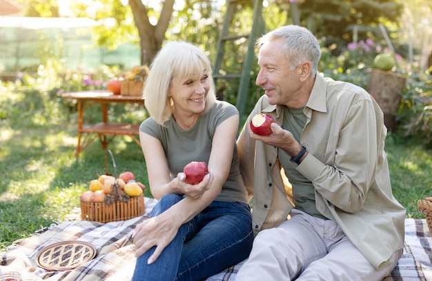 Gezonde en gelukkige pensionering positieve bejaarde echtgenoten die op gazon zitten en appels eten die in rusten