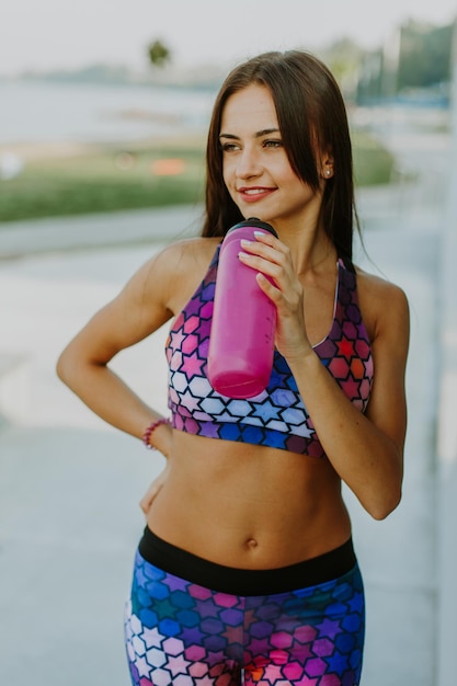 Gezonde en sportieve jonge vrouw die water drinkt uit de fles die buiten sport doet