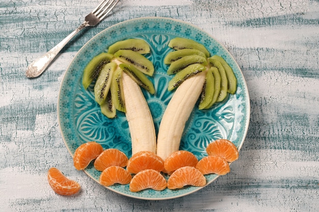 Gezonde fruitsalade voor kinderen van kiwi, bananen en mandarijnen in de vorm van een palmboom, bovenaanzicht