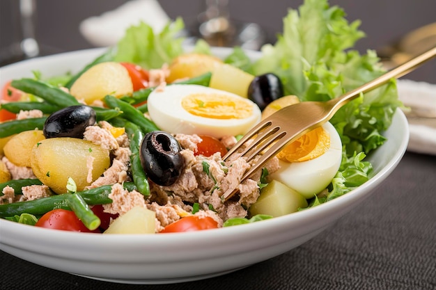 Gezonde, gezonde salade van tonijn, groene bonen, tomaten, eieren, aardappelen, zwarte olijven, close-up in een kom op tafel.