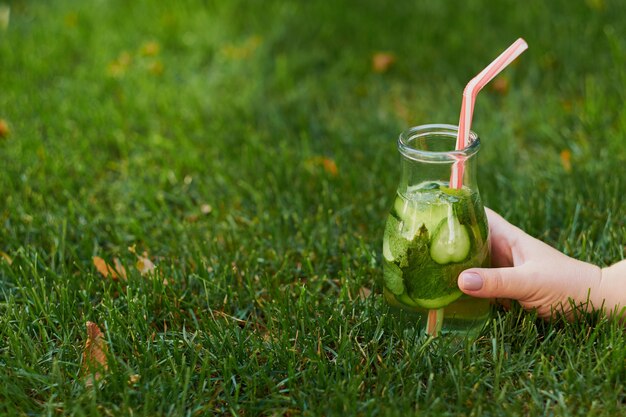 Gezonde groene detox-drank op zomergras in de hand. Verse koude theepot buitenshuis.