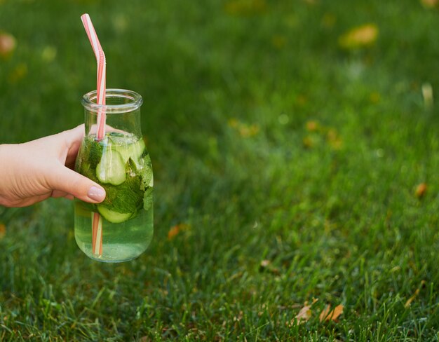 Gezonde groene detox-drank op zomergras in de hand. Verse koude theepot buitenshuis.