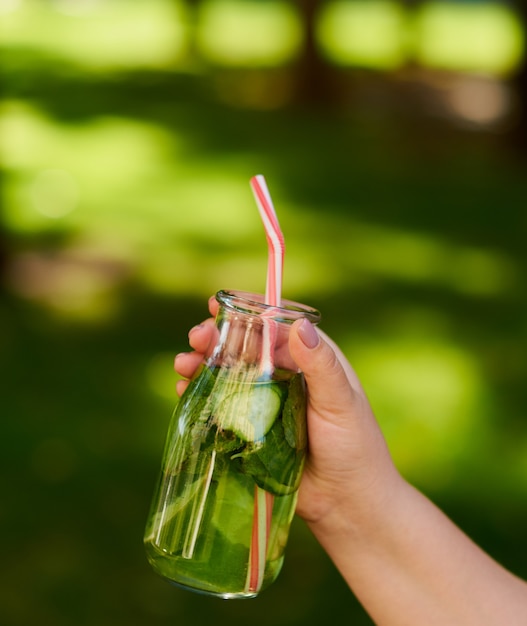 Gezonde groene detox-drank op zomergras in de hand. Verse koude theepot buitenshuis.