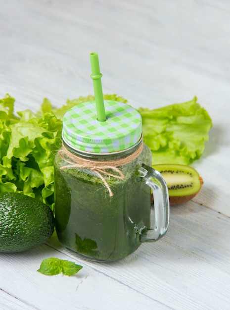 Gezonde groene smoothie met ingrediënten op witte houten lijst