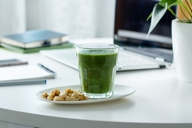 Gezonde groene smoothie van Spinazie, kiwi en noten op werkplek werktafel met laptop