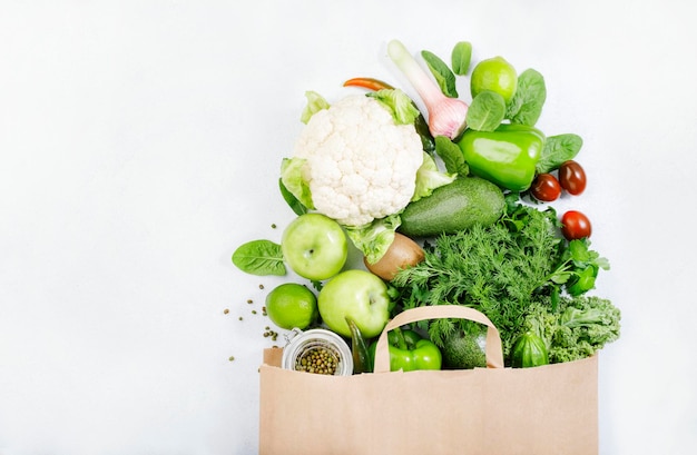 Gezonde groene veganistische vegetarische voeding in volle papieren zak groenten en fruit op witte achtergrond Winkelen voedsel supermarkt rauw detox dieet en schoon eten concept Gezonde voeding achtergrond