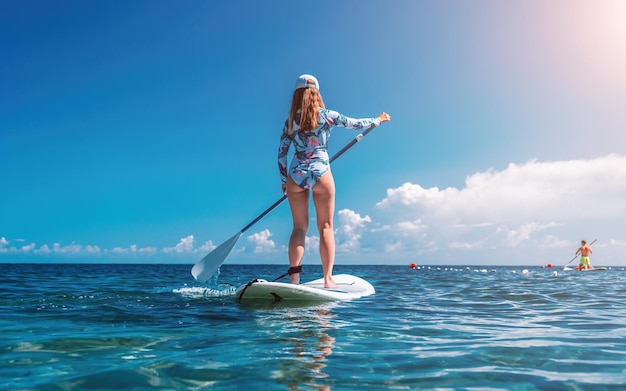 Gezonde happy fit vrouw in bikini ontspannen op een sup surfplank drijvend op de heldere turquoise zee