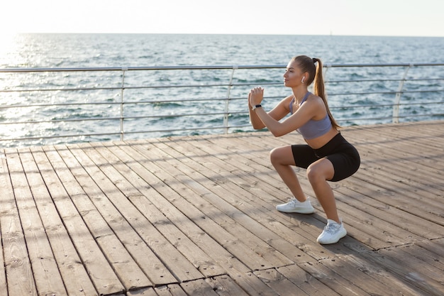 Gezonde jonge fitness vrouw doet squat oefening op het strand bij zonsopgang