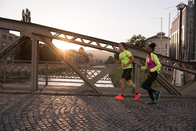 gezonde jonge multi-etnische paar joggen in de stad in de vroege ochtend met zonsopgang op de achtergrond