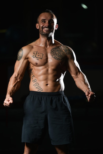 Gezonde jonge Tattoo Man permanent sterk In de sportschool en buigen spieren gespierde atletische Bodybuilder Fitness Model poseren na oefeningen