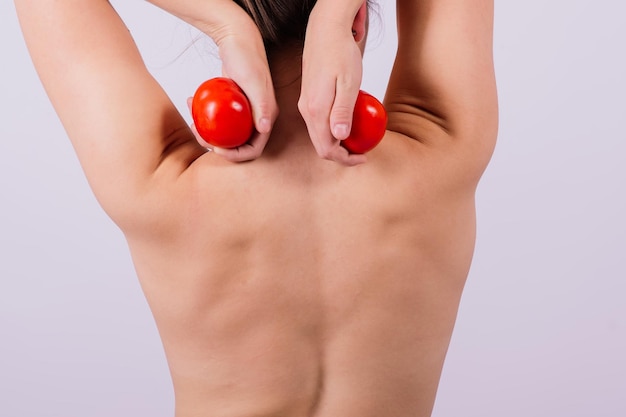 Gezonde jonge vrouw die tomaten voor haar ogen houdt en blote schouders topless lacht