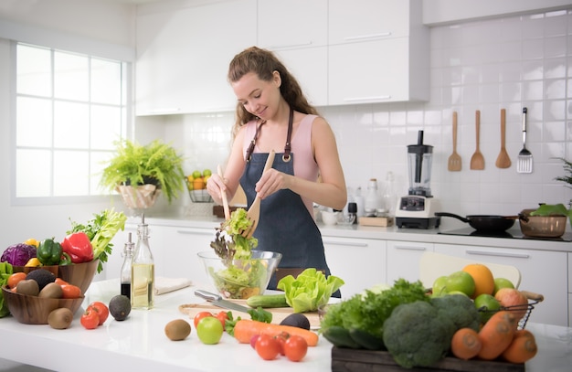 Gezonde jonge vrouw in een keuken die groenten voor gezonde maaltijd en salade voorbereidt