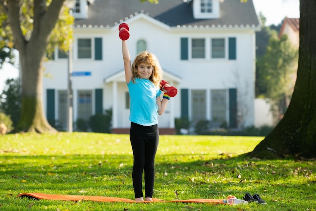 Gezonde kinderen leven en sport concept Portret van kind jongen trainen met halters buitenshuis Motivatie en sport concept voor kinderen Sport sterke jongen kleine bodybuilder