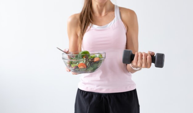 Gezonde levensstijl, mensenconcept - een bord salade in de ene hand en een halter in de andere hand. Glimlach en fitnesspak.