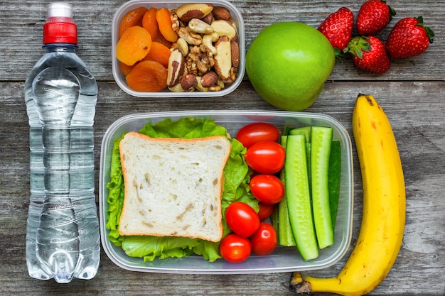 Gezonde lunchboxen met sandwich en verse groenten, flesje water, noten en fruit