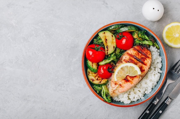 Gezonde lunchkom met gegrilde zalmrijst en groenten Gegrilde courgette-broccoli en tomaat met zalmsteak en rijst