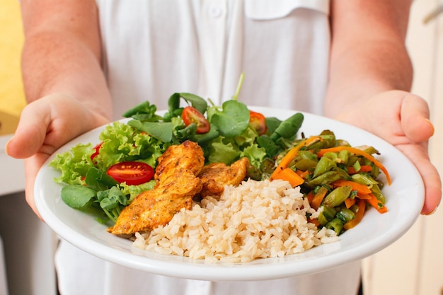 Gezonde maaltijd met gegrilde kip, rijstsalade en groenten geserveerd door vrouw