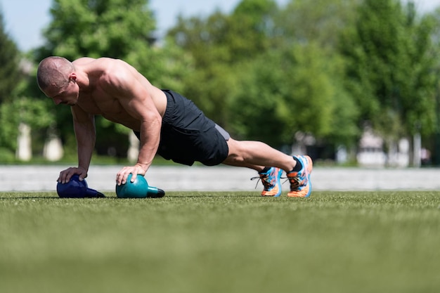 Gezonde man doet pushups op gras met Kettlebell