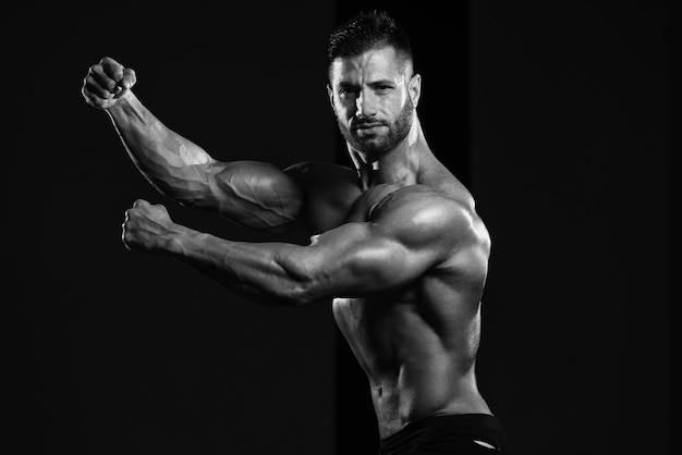 Gezonde man staat sterk in de sportschool en buigt spieren Gespierde atletische bodybuilder Fitness Model poseren na oefeningen