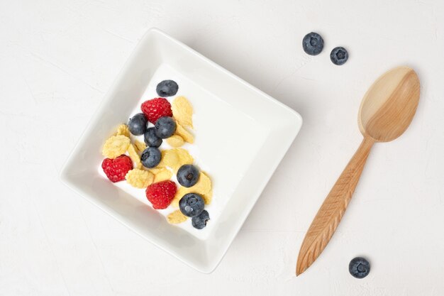 Gezonde ontbijtkom, cornflakes, yoghurt en verse bessen op een wit bord. Close-up, bovenaanzicht, geïsoleerde achtergrond. Concept van gezond en smakelijk eten.