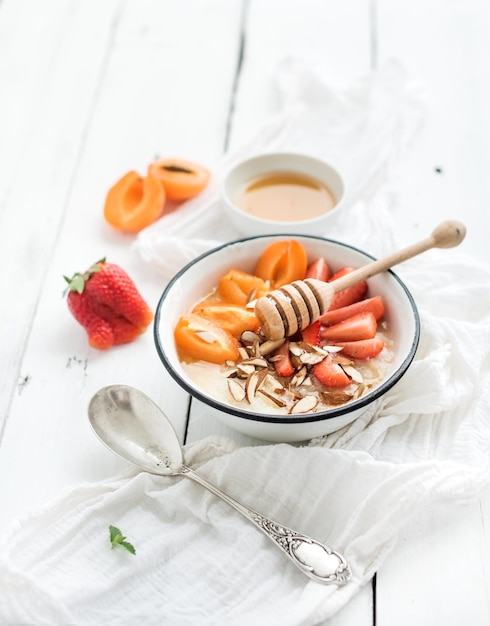 Gezonde ontbijtset Rijstgraan of pap met verse aardbeien, abrikozen, amandel en honing over een wit rustiek houten achtergrond bovenaanzicht