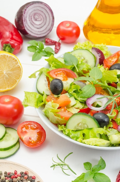 Gezonde salade met tomaten, komkommers en paprika's in een bord op een witte houten achtergrond