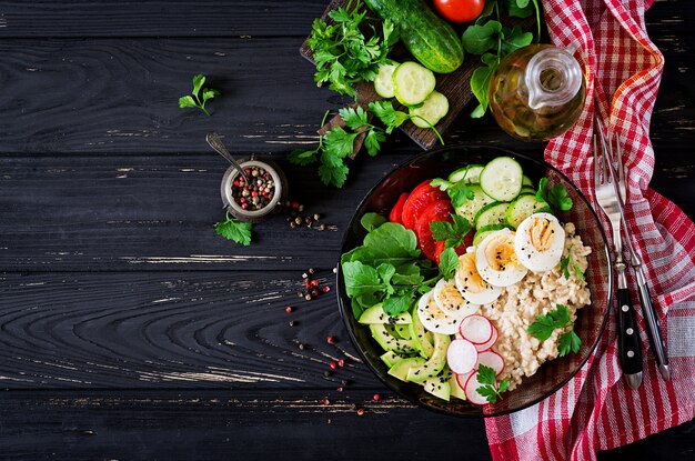 Gezonde salade van verse groenten - tomaten, avocado, komkommer, radijs, ei, rucola en havermout op kom. Diëet voeding. Plat leggen. Bovenaanzicht