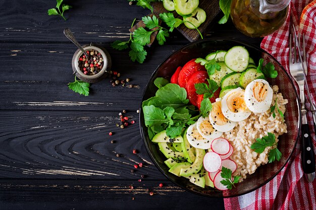 Gezonde salade van verse groenten - tomaten, avocado, komkommer, radijs, ei, rucola en havermout op kom. Diëet voeding. Plat leggen. Bovenaanzicht