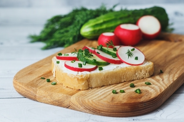 Gezonde sandwich met komkommer, radijs en roomkaas op een houten snijplank