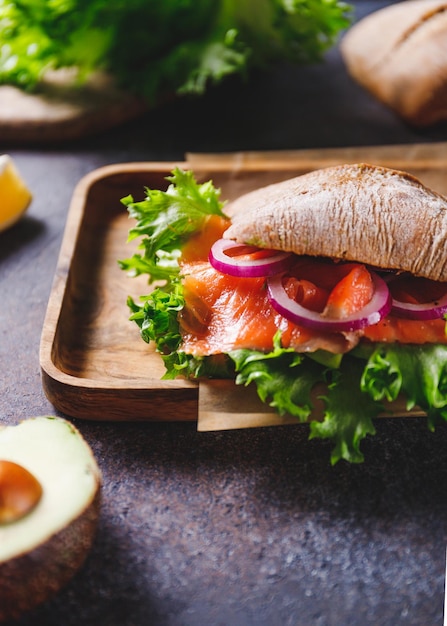 Gezonde sandwich met roggebrood broodje zalm avocado ui en salade geserveerd op een rustieke houten plank