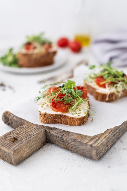 Gezonde sandwich met roomkaas gebakken tomaten en microgroenten op witte achtergrond Gezonde ontbijtsandwiches op een houten plank