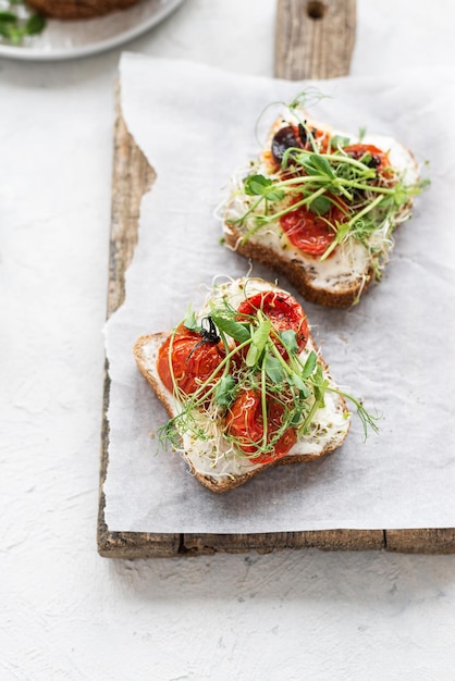 Gezonde sandwich met roomkaas gebakken tomaten en microgroenten op witte achtergrond