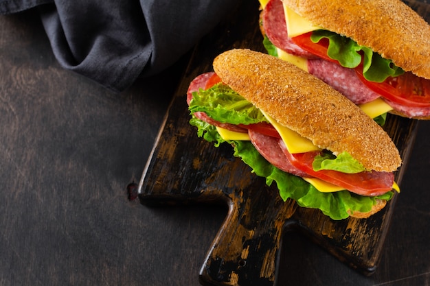 Gezonde sandwiches met zemelenbrood, kaas, groene sla, tomaat en gesneden salami op rustieke houten tribune. Ontbijt concept. Bovenaanzicht