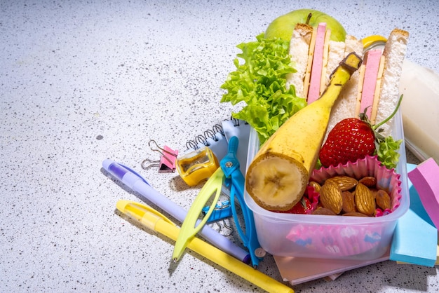 Gezonde school lunchbox boterham groenten fruit noten en yoghurt met school kinderen benodigdheden accessoires en rugzak op zwarte achtergrond flatlay kopieerruimte Terug naar school concept