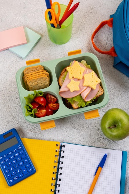 Gezonde schoollunchdoos met broodje en salade op de werkplek in de buurt van rugzak Schoolbenodigdheden boeken appel en een fles water