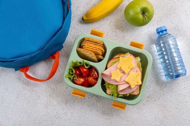 Gezonde schoollunchdoos met broodje en salade op de werkplek in de buurt van rugzak Schoolbenodigdheden boeken appel en een fles water