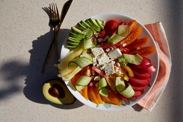 Gezonde seizoenssalade met rode, oranje en gele tomaten, paprika, avocado, komkommers, fetakaas, sesam onder harde schaduwen Natuurlijke biologische voeding, goede voeding