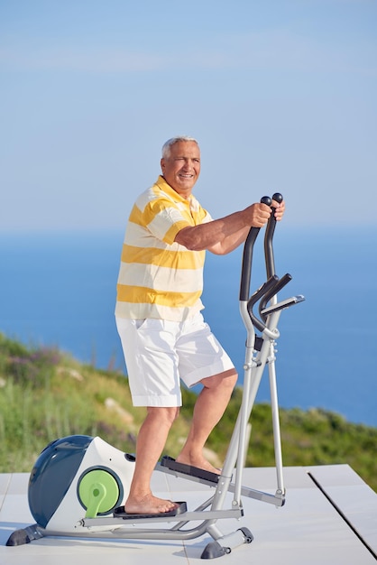 gezonde senior man die traint op een loopbandmachine op een modern huisterras met uitzicht op de oceaan