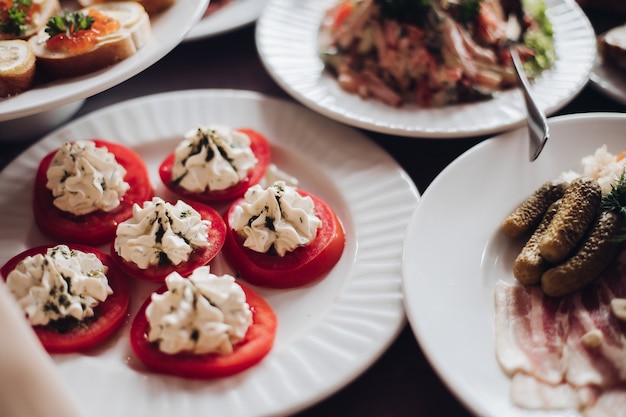 Gezonde smakelijke snacks op plaat. Gesneden tomaten met roomkaas en kruiden erop. Kerst- of nieuwjaarsbanket.