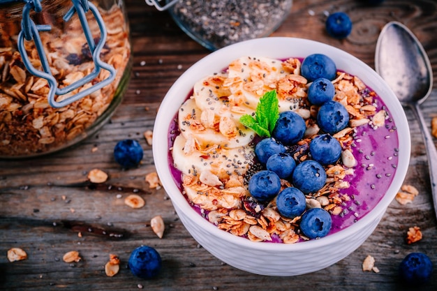 Gezonde smoothiekom met granolabanaan en verse bosbessen op houten achtergrond